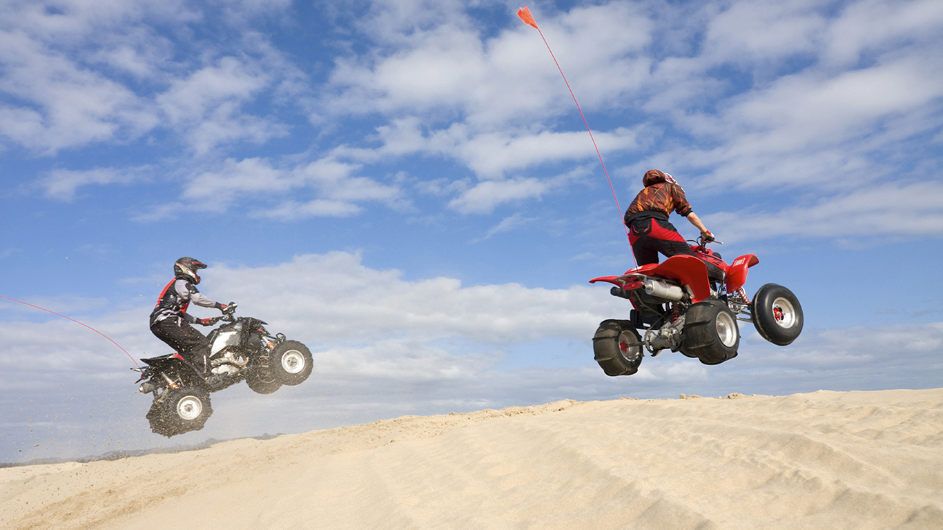 2 ATVS JUMPING OVER A DUNE ON THE BEACH